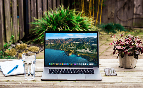 Laptop in yard displaying beautiful mountain image.
